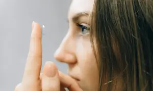 Zbliżenie na palec wskazujący z soczewką kontaktową przed okiem kobiety.