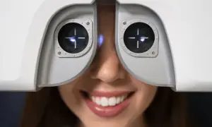 Uśmiechnięta kobieta podczas badania wzroku za pomocą urządzenia optometrycznego.